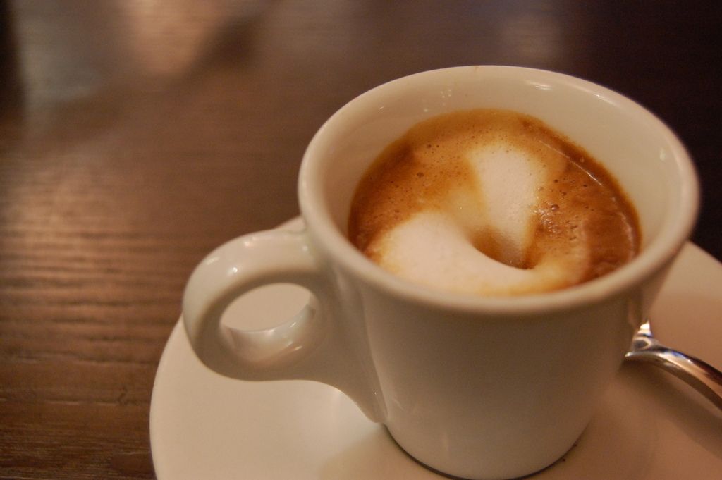 A cup of coffee with milky foam on a saucer on a wooden table